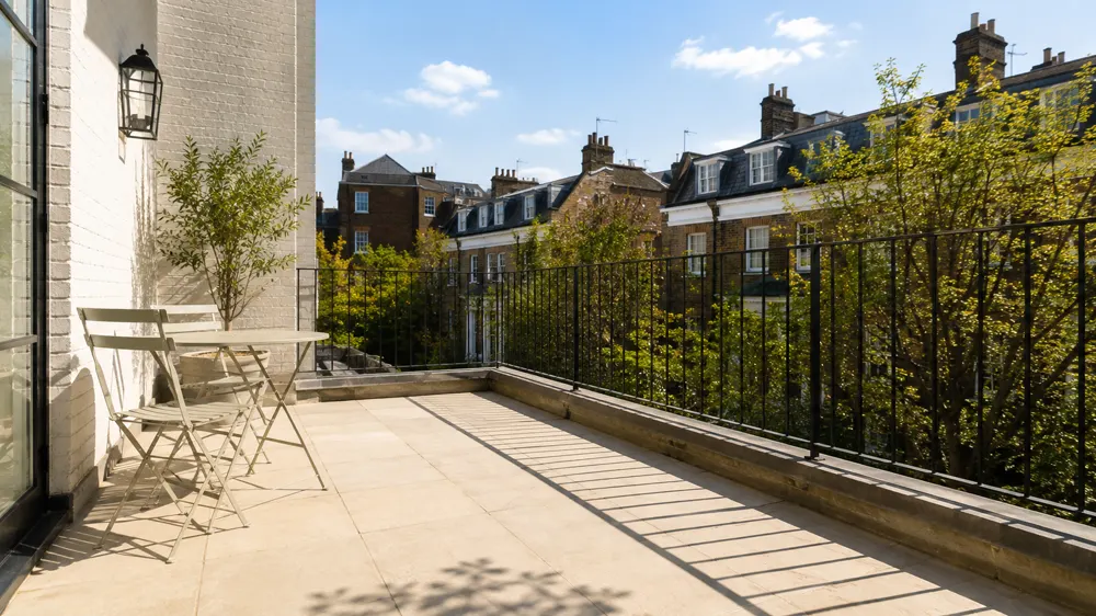 Wide scene: an open terrace in full afternoon sun, planting beside a table